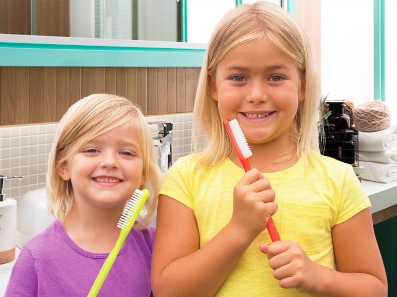 Two young girls holding big toothbrushes.